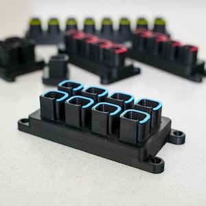 Könnte beinhalten: Ein schwarzer Kunststoff-Steckerblock mit mehreren blau umrandeten Anschlüssen. Der Block ist für elektrische Verbindungen konzipiert und hat eine rechteckige Form.