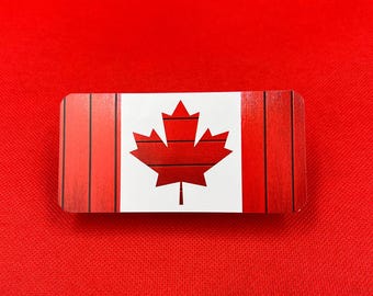 Op de afbeelding: Een rechthoekig houten bord met een rood-wit Canadees vlagontwerp. De vlag heeft een rood esdoornblad met een houtnerfstructuur.