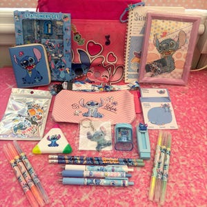 May include: A collection of Stitch-themed stationery items including a pink drawstring bag, a blue zippered wallet, a framed diamond art piece, a pencil case, a spiral notebook, stickers, a keychain, a pencil sharpener, pens, and pencils.