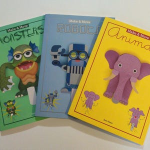 Peut inclure: Trois livres cartonnés colorés avec le titre "Make & Move" sur chaque couverture. Les couvertures présentent des illustrations d'un monstre, d'un robot et d'un éléphant. Le monstre est vert avec de grands yeux et un large sourire. Le robot est bleu et blanc avec une grosse tête et un corps avec des roues. L'éléphant est rose avec de grandes oreilles et une trompe.