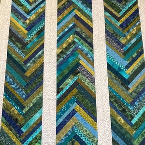 Peut inclure: Une courtepointe avec un motif en chevrons dans des tons de vert, bleu et jaune. La courtepointe est composée de nombreux morceaux de tissu différents cousus ensemble.