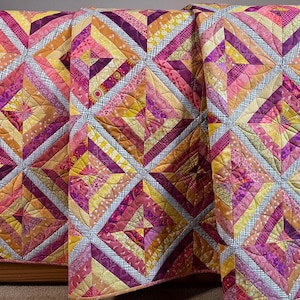 Könnte beinhalten: Ein farbenfroher Quilt mit einem geometrischen Muster. Der Quilt zeigt Quadrate mit Diamantenformen in Rosa-, Gelb-, Orange- und Lilatönen. Der Quilt besteht aus verschiedenen Stoffen und hat eine gesteppte Textur.