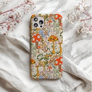 May include: A phone case with a colorful floral and mushroom pattern. The case features a cream background with orange, yellow, and blue mushrooms, along with white and yellow flowers. The case has a camera cutout.