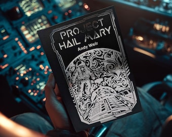 May include: A black book titled Project Hail Mary by Andy Weir with a silver foil illustration on the cover. The design features an astronaut floating in space above a complex mechanical structure, all framed by a geometric border.