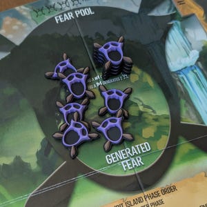 May include: A close-up of a board game with several purple and brown tokens. The tokens are shaped like stylized claws. The game board has text that reads "FEAR POOL" and "GENERATED FEAR".