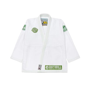 Puede incluir: Uniforme blanco de artes marciales con logotipos verdes y negros. El uniforme presenta el texto "SHOYOROLL" en verde. El uniforme tiene cuello en V y está diseñado para el entrenamiento de artes marciales.