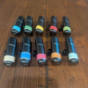 May include: A collection of ten black audio transmitters with colored bands. Each device has a different colored band, including blue, green, yellow, red, and orange. The text "BALILA" and "TX" are visible on each transmitter.