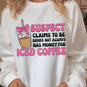 May include: White sweatshirt with a graphic of an iced coffee and the text "SUSPECT CLAIMS TO BE BROKE BUT ALWAYS HAS MONEY FOR ICED COFFEE" in pink and black. The iced coffee has a pink bow.
