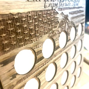 Puede incluir: Un tablero de madera clara con una bandera estadounidense grabada con láser y un gráfico de motocicleta. El texto dice LIFE IS A JOURNEY. Enjoy the ride. Contiene múltiples recortes circulares dispuestos en una cuadrícula para colocar objetos.
