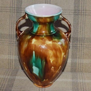 May include: A ceramic vase with two handles, featuring a glossy finish. The vase has brown, green, and yellow tones. The interior is light pink, and the rim is teal green. The vase is a classic shape, suitable for displaying flowers.