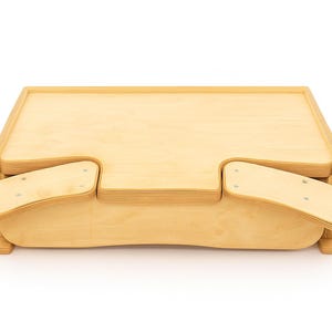 Puede incluir: Un escritorio de madera de color claro para portátil con dos extensiones laterales. El escritorio tiene una parte superior rectangular con bordes redondeados y dos reposabrazos que se extienden hacia afuera. Hecho de madera clara, está diseñado para cama o sofá.