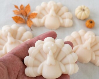 May include: Several off-white turkey-shaped soaps with detailed fan-shaped tail feathers and a wattle. The soaps are smooth and solid in colour, accompanied by small decorative orange pumpkins and dried orange leaves.
