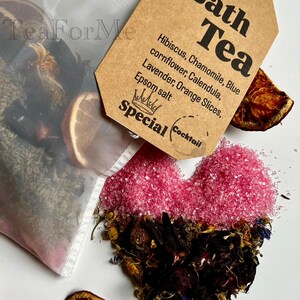 May include: A bath tea blend featuring a heart shape made of pink Epsom salt and dried flowers. A tag reads "Bath Tea" with ingredients listed. Includes orange slices and a tea bag.