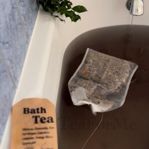 May include: A bath tea bag steeping in a bathtub. The bag contains herbs and flowers. A tag reads "Bath Tea" with the word "Special" at the bottom. The water is dark brown. The brand name "Tea For Me" is visible.