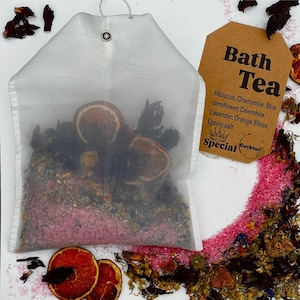 May include: A white mesh bath tea bag filled with dried herbs and orange slices. A brown tag reads "Bath Tea" with a list of ingredients. The ingredients include hibiscus, chamomile, blue cornflower, calendula, lavender, orange slices, and Epsom salt.