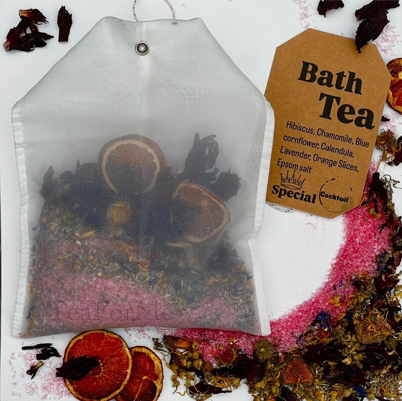 May include: A white mesh bath tea bag filled with dried herbs and orange slices. A brown tag reads "Bath Tea" with a list of ingredients. The ingredients include hibiscus, chamomile, blue cornflower, calendula, lavender, orange slices, and Epsom salt.
