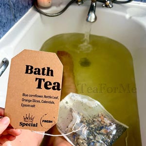 May include: A brown tag reading "Bath Tea" with ingredients listed: blue cornflower, nettle leaf, orange slices, calendula, and Epsom salt. A bath tea bag is held over a green-tinted bath. A lit candle and faucet are in the background.