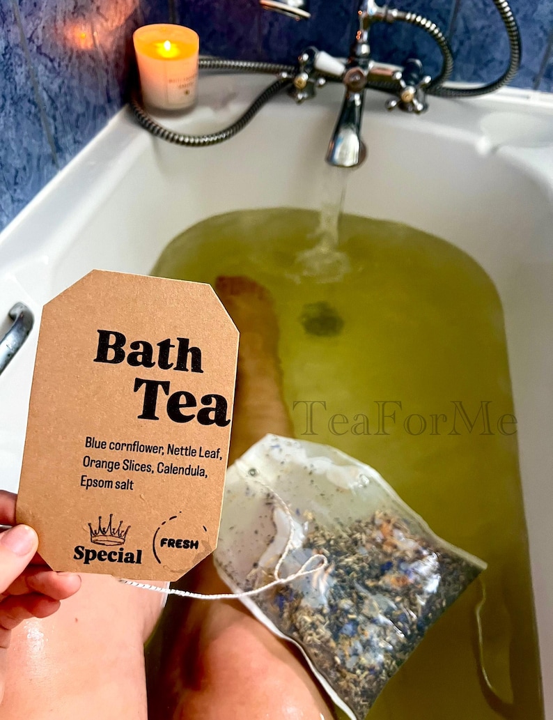 May include: A brown tag reading "Bath Tea" with ingredients listed: blue cornflower, nettle leaf, orange slices, calendula, and Epsom salt. A bath tea bag is held over a green-tinted bath. A lit candle and faucet are in the background.