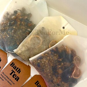 May include: Image of bath tea bags filled with dried herbs and flowers. The bags are in various shapes and sizes, some with tags that read "Bath Tea." Ingredients include blue cornflower, orange slices, and lavender. The text "Tea ForMe" is visible.