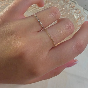 May include: A delicate chain ring featuring a two-tone design with a silver-colored section and a gold-colored section. The ring is constructed from small, interconnected oval links that form a thin, flexible band around the finger.