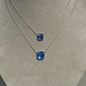 May include: A silver chain necklace with two blue gemstone pendants. The larger pendant is a square shape and the smaller pendant is a rectangular shape.