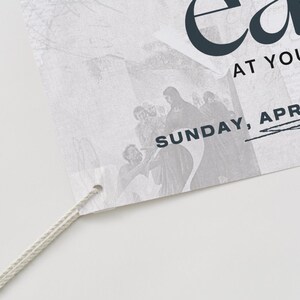 May include: A white poster with the word "Easter" in black text. The poster also includes the text "At Your Church" and "Sunday, April 20". The poster has a white string attached to it.