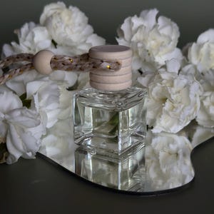 May include: A clear glass bottle with a wooden lid and a string hanging from it. The bottle is filled with a clear liquid and is surrounded by white flowers.