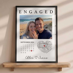 Könnte beinhalten: Ein gerahmter Wanddruck mit dem Wort ENGAGED, einem Foto eines Paares am Strand, einem Kalender für September 2026 mit dem rot markierten 26., einer herzförmigen Karte von Hyde Park, London, sowie den Namen Chloe und James mit einem Herz.