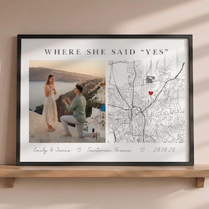 Puede incluir: Una lámina enmarcada con el texto WHERE SHE SAID YES en la parte superior. La izquierda muestra una fotografía de una pedida de mano en Santorini, Grecia. La derecha muestra un mapa de calles en blanco y negro con un corazón rojo. El texto inferior dice Emily & James, Santorini, Greece, 28.08.26.