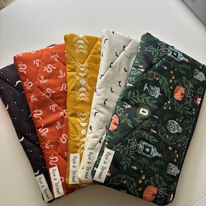 May include: Five rectangular quilted fabric pouches arranged in a fan shape. Each pouch features a unique print: black with moons, orange with snakes, mustard yellow with moon phases, white with bats, and dark green with potion bottles and pumpkins.