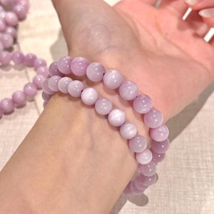 May include: Two lavender beaded bracelets. Each bracelet is made of round, polished beads. The bracelets are worn on a wrist. The beads have a soft, matte finish and a consistent color throughout.