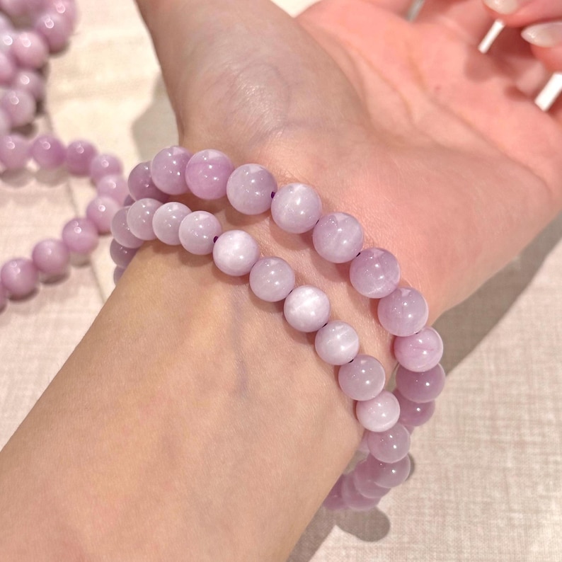 May include: Two lavender beaded bracelets. Each bracelet is made of round, polished beads. The bracelets are worn on a wrist. The beads have a soft, matte finish and a consistent color throughout.