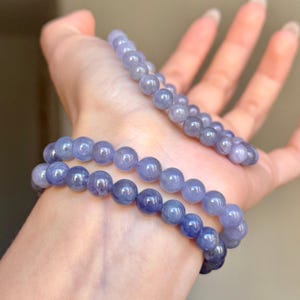 以下が含まれることがあります： 滑らかで丸い半透明の薄紫色のビーズで構成された2本のストレッチブレスレット。ビーズは磨かれた仕上げで、淡いラベンダー色からより深いバイオレットトーンまで、ストランド全体に微妙な色の変化が見られます。