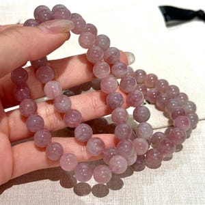 May include: A collection of light purple gemstone bead bracelets. The round beads have a translucent appearance. The bracelets are held in a hand, highlighting the colour and texture of the stones. The bracelets are a soft, muted purple colour.