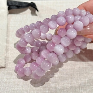 May include: Three light purple beaded bracelets. Each bracelet is made of round, polished beads. The bracelets are held together, showing the elastic band. The beads are a soft, pastel purple color. The bracelets are displayed on a light-colored surface.