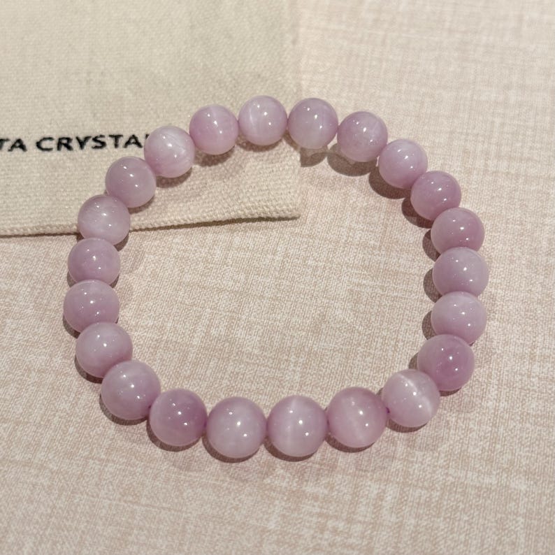 May include: A light purple beaded bracelet. The bracelet is made of round, polished beads. The beads are strung together on an elastic band. The bracelet is displayed on a neutral-colored surface.