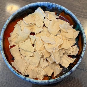 May include: A ceramic bowl with a dark blue rim, a red-orange center, and a light brown interior. The bowl is filled with irregularly shaped, light tan pieces, possibly food items like crackers or chips.