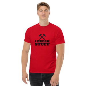 Pode incluir: Camiseta vermelha de manga curta com um gráfico preto de dois martelos cruzados e o texto "I BREAK STUFF".