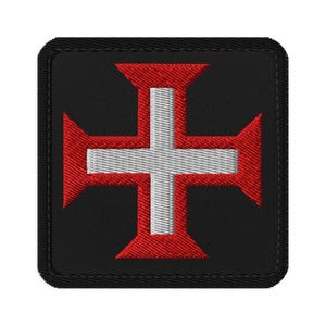 May include: A square embroidered patch featuring a black background with a centered red cross pattée. A smaller white cross is layered over the center of the red cross. The patch has a black stitched border with rounded corners and a textured finish.
