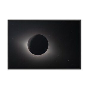 May include: A black and white framed print depicting a solar eclipse. The image shows the dark silhouette of the moon in front of the sun, surrounded by a bright corona. Stars are visible in the background.