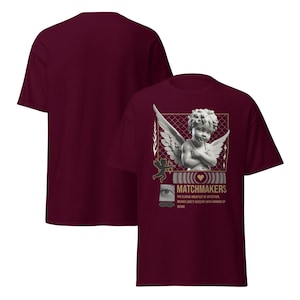 May include: Burgundy t-shirt featuring a graphic of a cherub with wings, a heart, and the text "MATCHMAKERS". The design includes gold accents and additional text. The shirt is a short-sleeved, crew neck style.