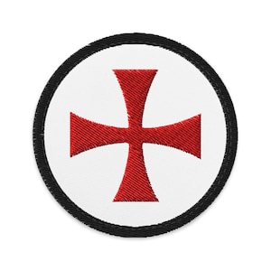 May include: Circular embroidered patch with a red cross emblem on a white field, framed by a black border. The patch is designed for attachment to garments or accessories, with a detailed stitch.