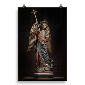 May include: A detailed, full-length statue of an angel with golden wings, holding a cross-topped staff. The angel is dressed in robes of red, blue, and gold, standing atop a serpent. The background is a dark brick wall.