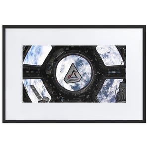 May include: Framed print showing a view from a spacecraft window, with Earth's atmosphere and clouds visible. The Artemis logo is in the centre. The frame is black, and the print is matted in white.