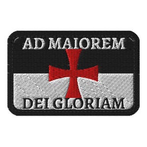 May include: A rectangular embroidered patch featuring a horizontal split design with a black upper half and a white lower half. A red cross is centered over the split. The white text AD MAIOREM is at the top and DEI GLORIAM is at the bottom.