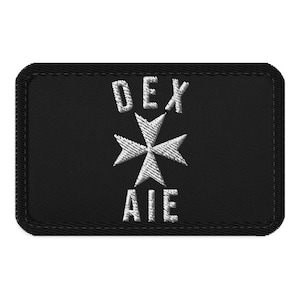 May include: A rectangular black embroidered patch with a stitched border. The design features the white text DEX above a white Maltese cross symbol, with the white text AIE positioned directly below the cross, all centred on the black fabric.