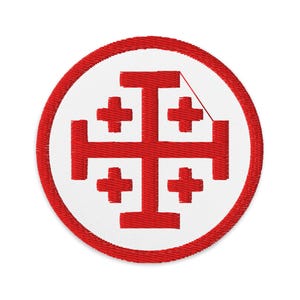 May include: A circular patch with a red Jerusalem cross emblem on a white backdrop, framed by a red border. The patch appears to be embroidered, with visible stitch detailing. The design is centrally positioned and symmetrical.