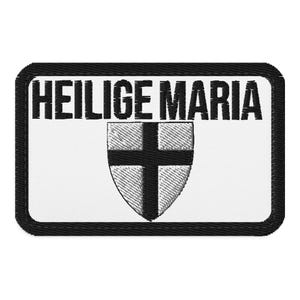 Puede incluir: Un parche rectangular bordado con fondo blanco y un borde negro grueso. El texto HEILIGE MARIA está bordado en letras mayúsculas negras sobre un emblema en forma de escudo que presenta una cruz negra sobre un fondo blanco.