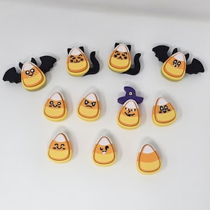 Puede incluir: Una colección de decoraciones temáticas de Halloween con diseños de caramelos de maíz. Algunas piezas de caramelo de maíz tienen orejas de gato, alas de murciélago o sombreros de bruja. Las piezas de caramelo de maíz tienen varias expresiones faciales y son amarillas, naranjas, blancas y negras.