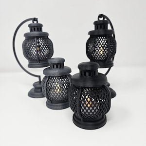 Pode incluir: Quatro lanternas de metal preto com um design de treliça decorativo. As lanternas são de tamanhos diferentes e são iluminadas por pequenas velas.